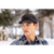 Young man in a winter scene with trees in the background. Man is wearing a dark Stormy Kromer cap and a dark blue plaid flannel Stormy Kromer shirt.
