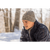 Close up photo of a young man crouched down in the snow and looking off in the distance. He is wearing a charcoal Watch Cap and a navy plaid wool jacket.