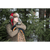 Image of a man leaning on a traditional wooden snowshoe in front of evergreen trees. He is wearing a red/black plaid Trapper Hat and and olive green quarter zip.