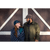 Photo of man and woman standing side by side and turned to face each other in front of brown and white barn doors. Man is wearing Stormy Kromer Insulated Waxed Cotton Cap in dark oak and olive wool coat, woman is wearing blue and green plaid hat with gray and black check blanket wrapped around her.