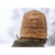 Close-up, back image of a man wearing a Stormy Kromer Marsh Cap with the earflaps folded down and the Stormy Kromer signature in view on the back. The background is very snowy.