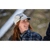 Photo of a laughing woman with long red hair looking to the side with blurry trees in the background. She is wearing a white Sidekick Cap and a blue plaid overshirt.