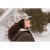 Photo of a woman with long dark hair standing outside in winter and looking to the side. She is wearing a fawn plaid Sidekick Cap and a brown plaid hooded jacket.