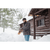 Photo of a man walking out from a log cabin in a very snowy scene. He is pulling on olive mittens and is wearing a dark Stormy Kromer Cap, North Star Plaid Mackinaw Coat and jeans.