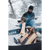 Photo of a man adding a log to an outdoor fire pit, surrounded by snow. Man is wearing a dark Stormy Kromer cap with the earband pulled down, a green Forge Quarter Zip and dark oak mittens.