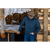 Photo of a man standing in front of a large log pile with his head down. He is wearing a dark oak Stormy Kromer cap, a navy Forge Quarter Zip and jeans.
