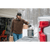 Photo of a man loading the back of his pick up truck with a bucket for ice fishing. It is snowing and the garage can be seen in the background. He is wearing a camouflage Stormy Kromer Cap, a brown Forge Quarter Zip and gray mittens.