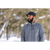 Photo of a man standing in front of snowy trees and looking to the side. He is wearing a blue Stormy Kromer Cap and a charcoal Forge Quarter Zip.