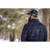Image from the back of a man standing in front of a row of snowy trees, wearing a plaid Stormy Kromer Cap and an indigo Boundary Jacket.