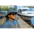 Image of a smiling man in sunglasses seated along a marina, with a boat in the background. He is wearing a charcoal Forager Hat and a blue tee shirt.
