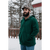 Image of a bearded man in his 30s standing in the snow in front of a railing wearing a green Stormy Kromer Tailgate Pullover and a plaid wool Stormy Kromer cap.