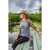 Photo of a woman sitting on a bench on a dock with the lake in the background. She is looking off to the distance and is wearing a gray and green baseball tee and The Mesh Hiker hat in Khaki.
