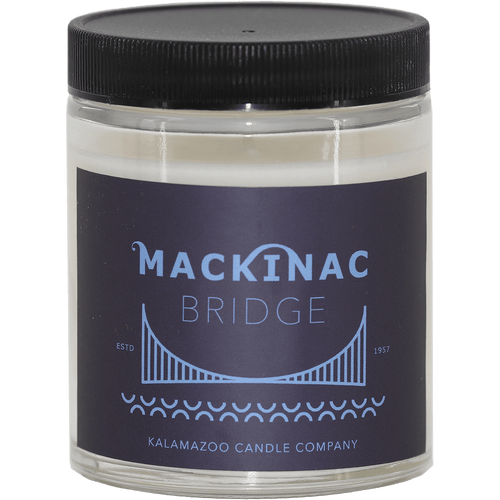 Glass jar candle from Kalamazoo Candle with black lid and label, printed with a Mackinac bridge drawing in light purple