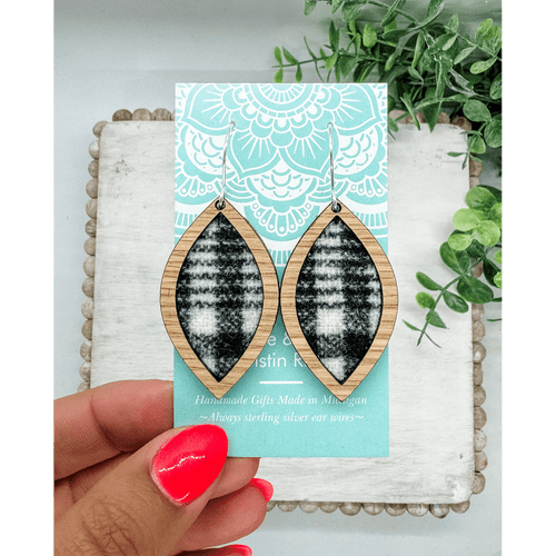 Pair of leaf shaped earrings made of a light wood framing black and white wool fabric