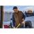Man wearing a brown waxed Crew Vest with a truck with a snowplow on the front.