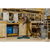 Older man wearing a brown waxed Crew Vest sweeping in his woodshop.