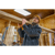 Man in a woodshop wearing a gray wool Compass Shirt Jack carrying a long board on his shoulder.